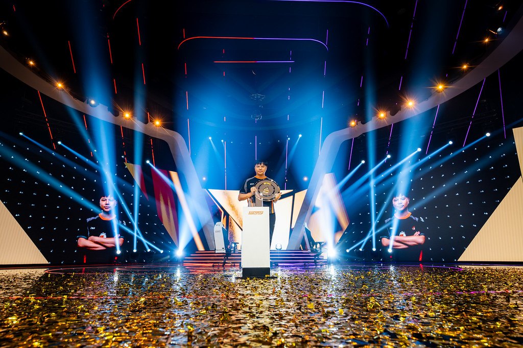A champion lifts the trophy on the Esports World Cup main stage amid gold confetti and stage lighting