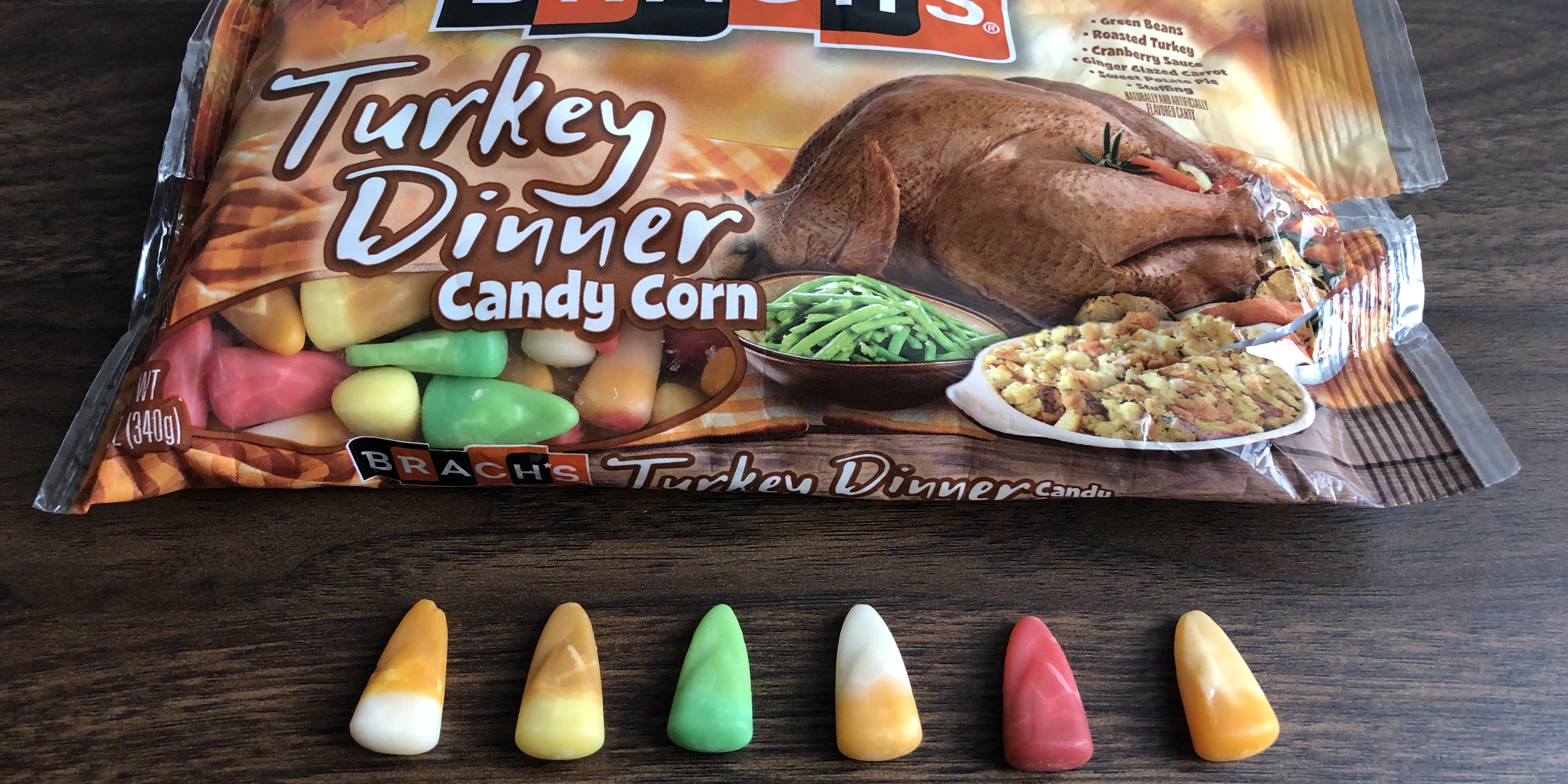 A bag of Brach's Turkey Dinner Candy Corn with individual pieces lined up in front of it, part of the Halloween seasonal candy category.